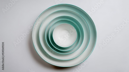 Four white ceramic bowls with teal rims nested inside each other on a light background.