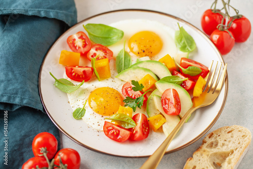 Healthy breakfast. Fried eggs and vegetables - cherry tomatoes, avocado slices, spinach leaves, sweet pepper and parsley in plate on the table