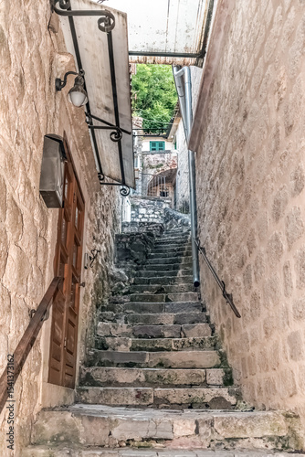 Narrow stone steps leading through a rustic passage in the old town of Kotor, Montenegro. The worn stairs and surrounding stone walls showcase the historic charm of this medieval town