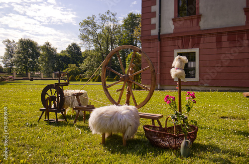 Traditional wooden spinning wheel for spinning yarn from sheep's hair. Ancient tool for making yarn. Spinning wheel, old craft. In the background the castle garden.