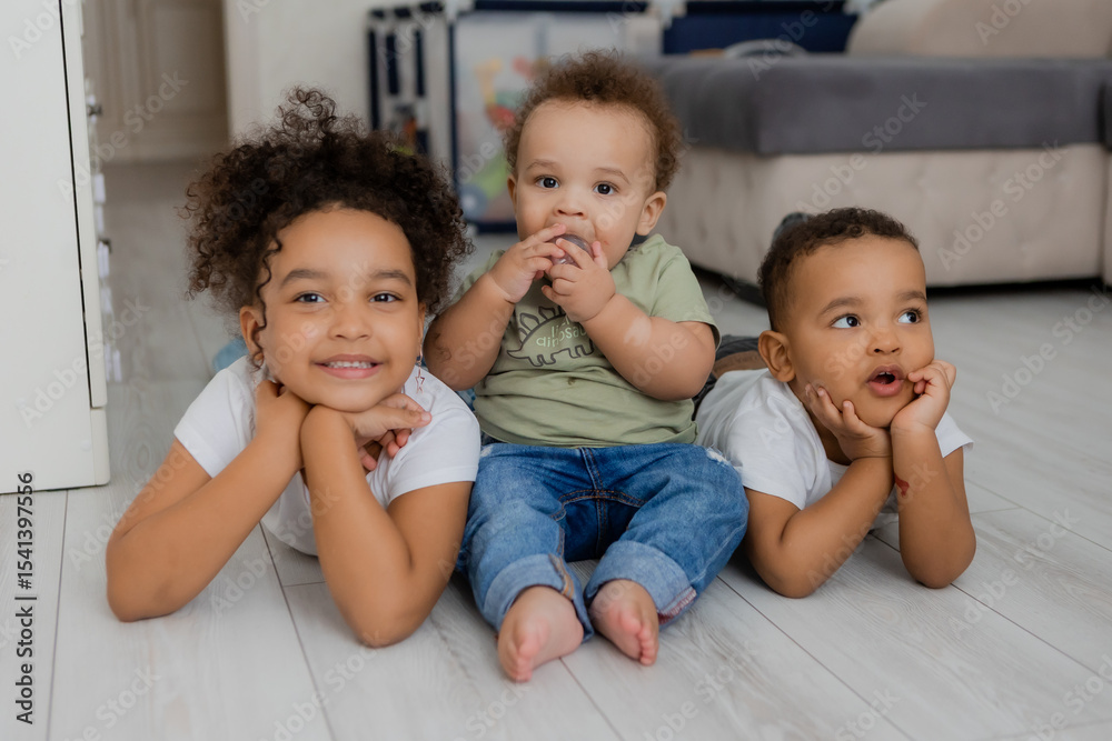 three African-American children lie on the wooden floor of a house three African-American children lie on the wooden floor of a house