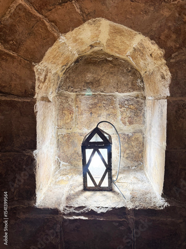 Vintage lantern glowing in arched stone niche with textured medieval wall and soft shadows