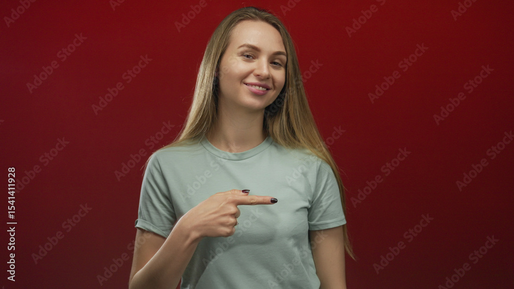 Woman smiling with long hair pointing on an isolated red background showcasing confidence and highlighting a casual friendly demeanor Woman smiling with long hair pointing on an isolated red background showcasing confidence and highlighting a casual friendly demeanor