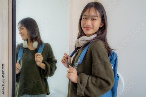 Portrait of Asian schoolgirl packing her backpack and getting ready for school. Elementary student preparing at home, showing childhood routine and back-to-school education concept.
