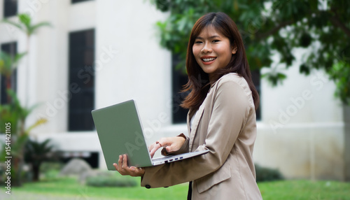 Portrait happy Asian businesswoman working on laptop in city. 