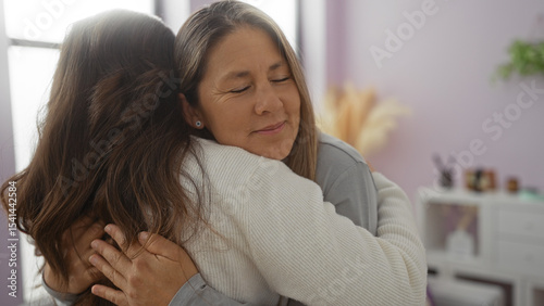 Obraz na plátně Mother and daughter embrace lovingly in a cozy living room, capturing a moment of family affection indoors