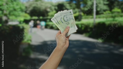 Man holding singapore dollars on a sunny street highlights money and outdoor activity in a city setting.