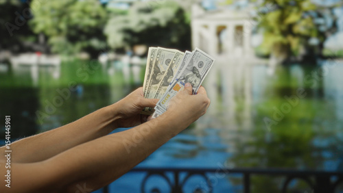 Man holding american banknotes outdoors in a garden setting, highlighting the concept of finance and currency exchange in a tranquil park environment.