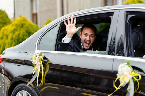 Cheerful groom or guest waving from a decorated wedding car.
