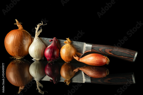 Various fresh onion types arranged with chef's knife on reflective black surface, perfect for culinary and cooking themes