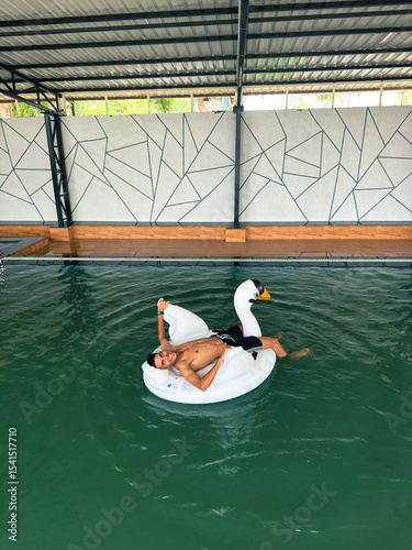 Young Man Relaxing on Swan Float in Indoor Pool