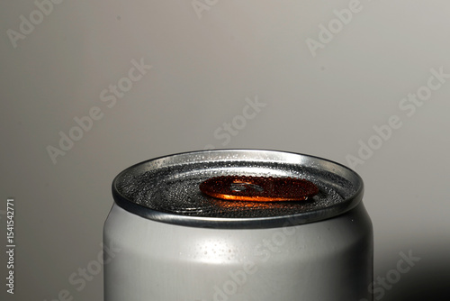 Close-up photo of a silver soda can top with an orange pull tab and condensation droplets, soft shadow on neutral background.

