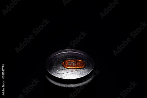 Close-up macro photo of a silver soda can top with an orange pull tab and water droplets, dark background, high contrast detail.

