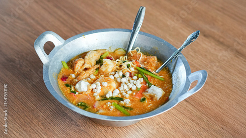 Seblak with vegetables and assorted toppings in a pan on wooden table side view