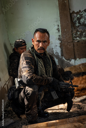 Brave soldier standing in ruined abandoned building with rifle in hands and shooting at opponent towards camera. In background is his fellow team ready for rescue mission and operation