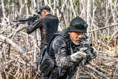 A group of military men in combat gear patrol in the middle of tropical jungle.