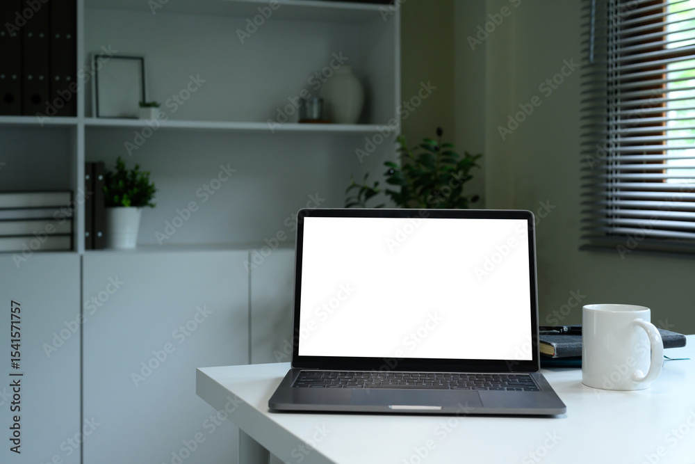Fototapeta premium Modern workspace with blank laptop screen, coffee mug, and books on a white desk