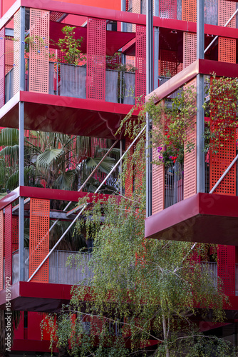 Red building structure with integrated vertical gardens and hanging plants, Montpellier, France, combining bold design and environmental responsibility