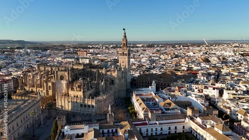 Aerial view of a historic cathedral with a tall bell tower in a cityscape at sunset.