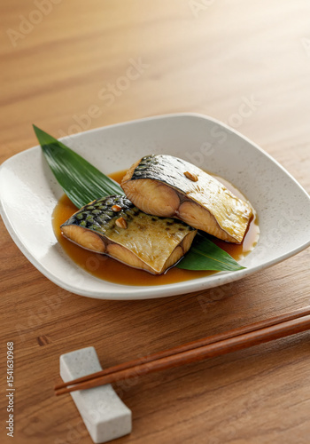 Traditional simmered saba fish in sweet soy sauce served on ceramic dish with bamboo leaf and wooden chopsticks