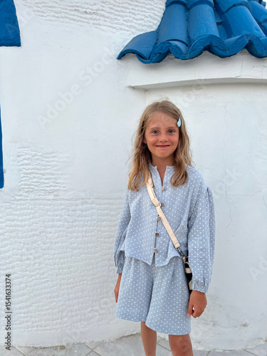 Smiling Little Girl in Light Blue Outfit Against White Greek Architecture