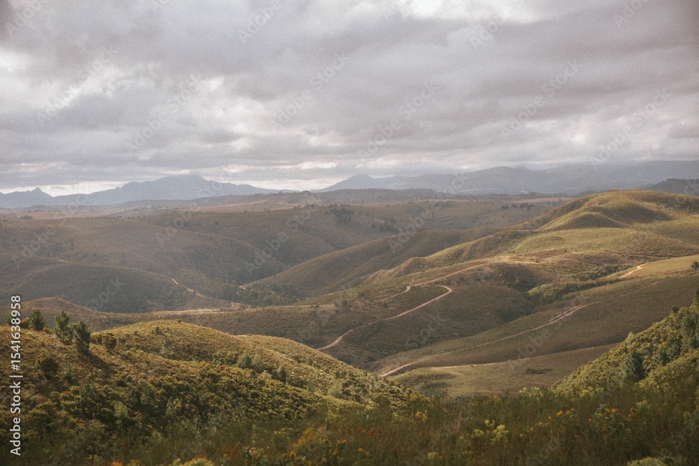 Fototapeta premium Scenic view of rolling hills under a cloudy sky.