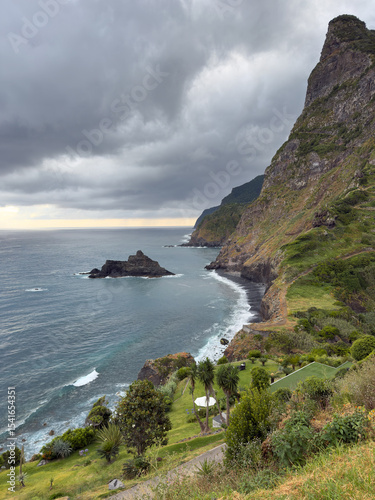 Rugged coastline of Madeira Island in Portugal is constantly exposed to ocean waves. Picturesque green shore features pristine white waves and impressive view of jagged stones.