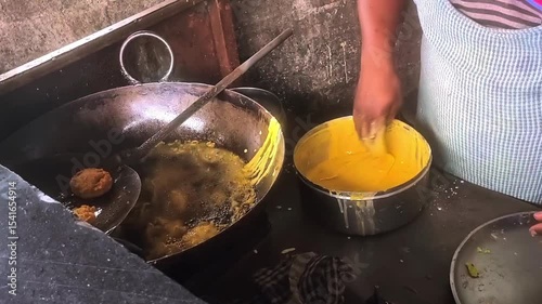 A man making vadapav by picking batata vada dip in besan batter and putting in frying pan with boiling oil. Vadapaav is famous indian dish which mostly pupular in mumbai maharashtra.