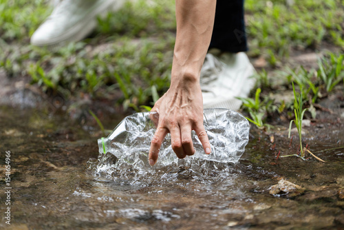 Volunteer action. Individual retrieving plastic bottle from river.