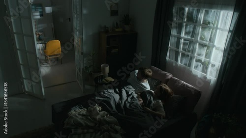 Wide angle shot of man and woman sleeping in bed under eerie moonlight when doors opening and furniture start moving on its own scaring couple by paranormal phenomena in apartment at late night