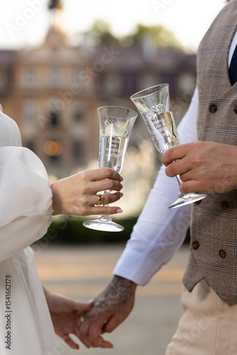 Two wedding glasses with engraving in the hands of the newlyweds against the background of the castle. Crystal champagne glasses in the hands of a couple in love.