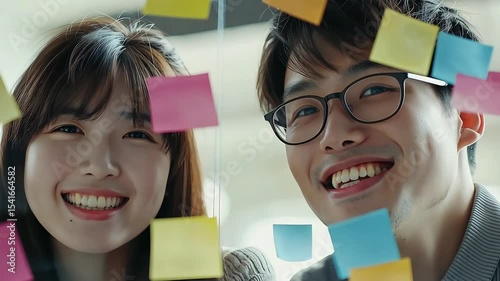 Two cheerful Asian students with sticky notes on their faces, a symbol of teamwork