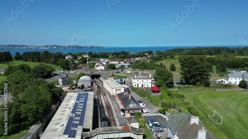 Churston, South Devon, England: DRONE VIEWS: A steam train slowly pulls into Churston railway station; the sea of Torbay is in the background. South Devon is a popular UK holiday destination.
