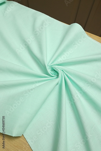 Flat lay of a mint green, lightweight linen fabric on the table. The soft, natural texture embodies craftsmanship, tailoring, and timeless textile artistry.
