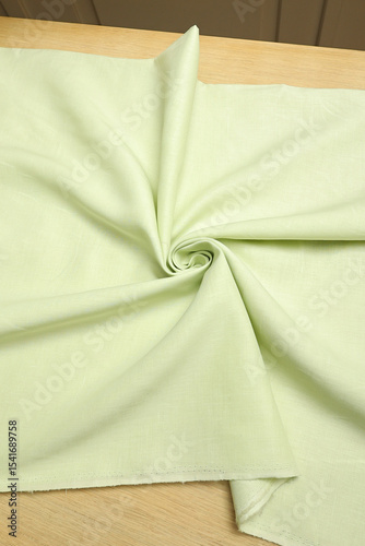Flat lay of a mint green, lightweight linen fabric on the table. The soft, natural texture embodies craftsmanship, tailoring, and timeless textile artistry.