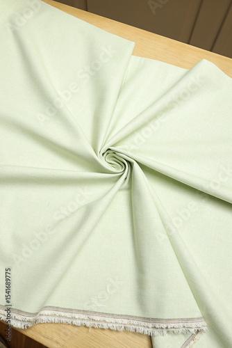 Flat lay of a mint green, lightweight linen fabric on the table. The soft, natural texture embodies craftsmanship, tailoring, and timeless textile artistry.