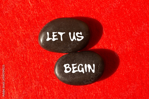 Let us begin message written on black stones on red background. Conceptual let us begin symbol. Copy space.