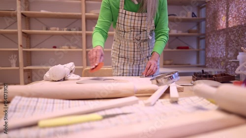 Skilled potter carefully cutting circular clay section using specialized circular cutter while working inside ceramic workshop, demonstrating precise crafting technique with professional movements