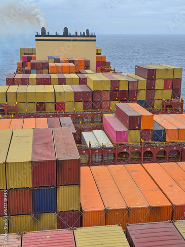 A large cargo ship laden with colorful shipping containers on the open ocean with smoke from the funnel, concept of global trade, logistics, maritime transport