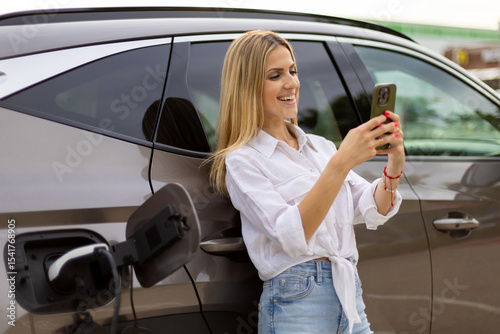 Businesswoman using smartphone while charging electric car at station