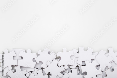 Different many white puzzle pieces on light gray table background. Closeup. Empty place for text. Top down view.