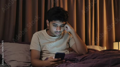 Indian Man Uses Phone While Lying in Bed at Night, Looking Worried