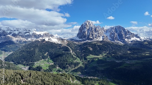 Drone photo of a spiky mountain with snow, forest in the foreground, sky and clouds in the background. shot in 4K in the dolomites, italy