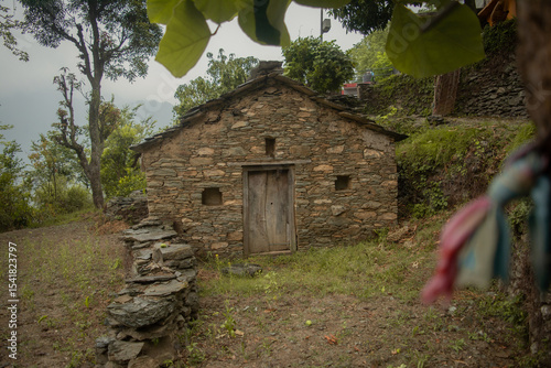 Centered view of an old abandoned house built with stone in a forest clearing, showcasing traditional Himalayan village architecture.