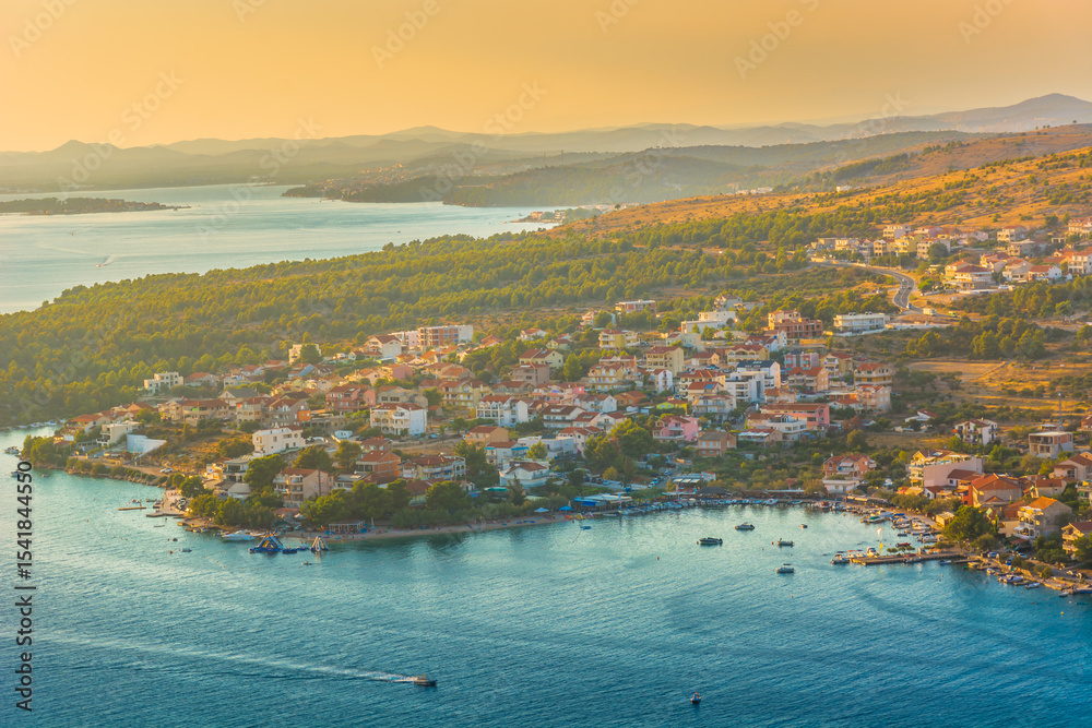 Fototapeta premium Aerial view of the coastal village of Grebastica near Sibenik, Croatia, featuring a deep bay, turquoise Adriatic waters, and lush Mediterranean surroundings in the Dalmatian region