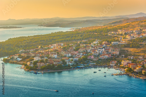 Aerial view of the coastal village of Grebastica near Sibenik, Croatia, featuring a deep bay, turquoise Adriatic waters, and lush Mediterranean surroundings in the Dalmatian region