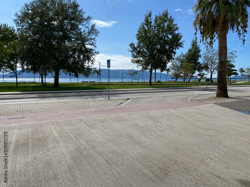 View of asphalt road against blue sea and green vegetation in Albanian city. Concept of rest and vacation in Mediterranean country. Photo for your article