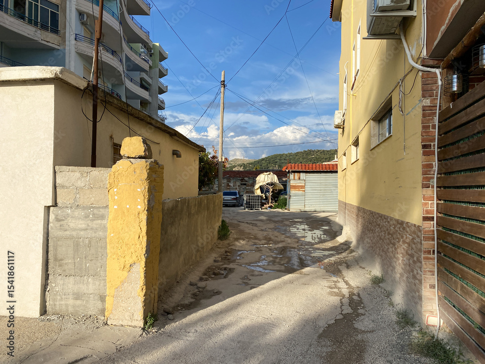 Obraz premium Typical day in a local Albanian neighborhood: old rooftops, narrow road, utility poles, and surrounding plants. The kind of everyday setting that quietly speaks of tradition and time.