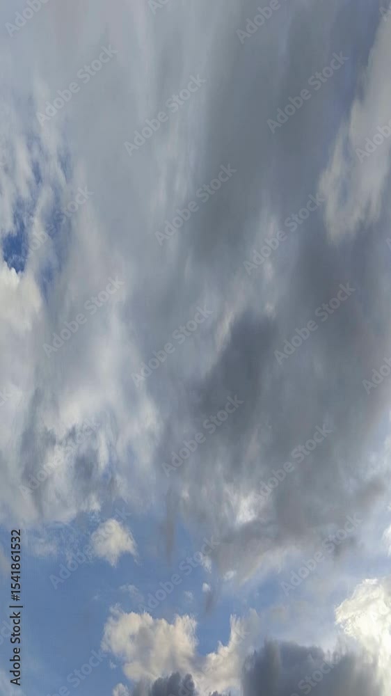Un cielo de azul con varias nubes de color blanco y gris con un movimiento lento. Video vertical