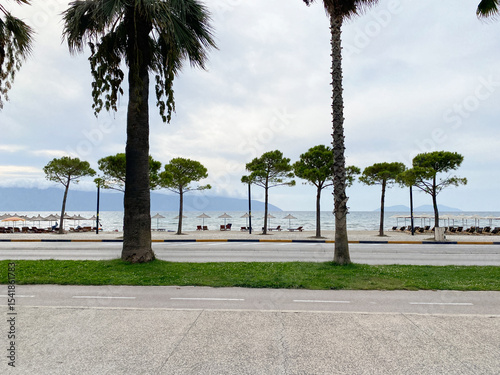 Asphalt road curves through green hills with the sea sparkling in the background. Mediterranean vibe in an Albanian city. Inspiring photo for designs about travel, freedom or nature.